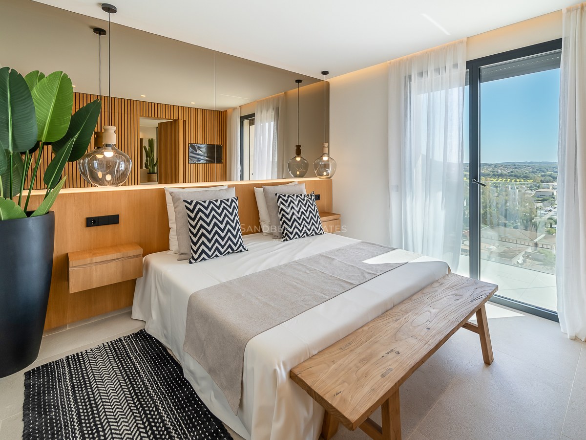 Chambre moderne avec tête de lit en bois, miroir mural, banc en bois et baies vitrées ouvrant sur une terrasse.