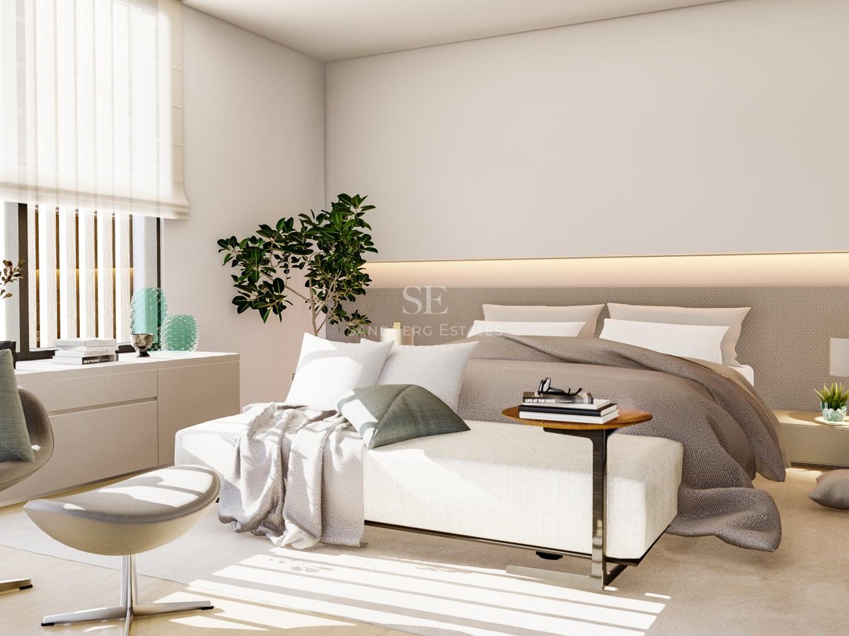 Modern bedroom with large bed, designer lounge chair, and natural light filtered through horizontal blinds.