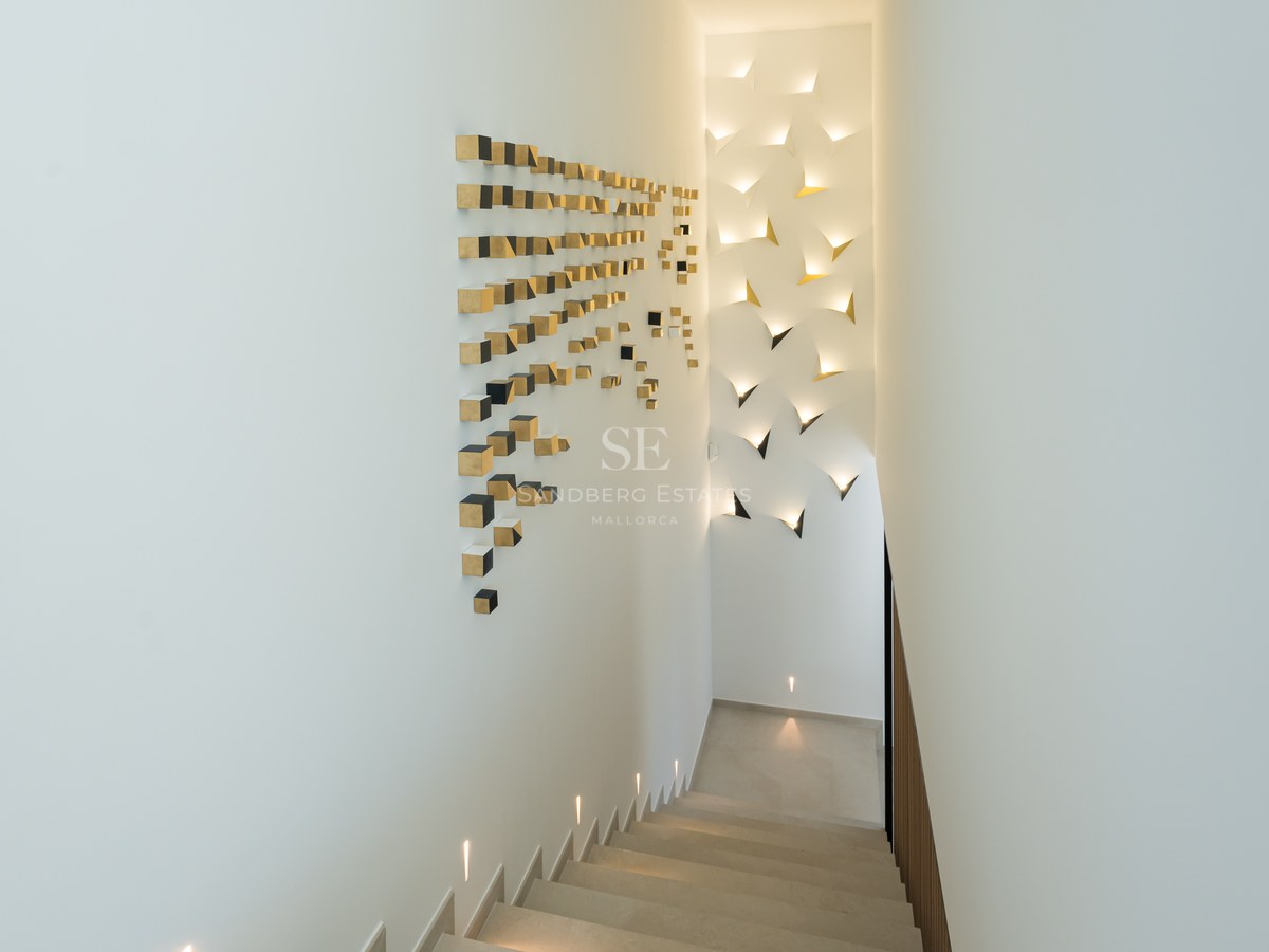 Modern minimalist staircase featuring integrated LED wall lighting and gold geometric art on white walls.