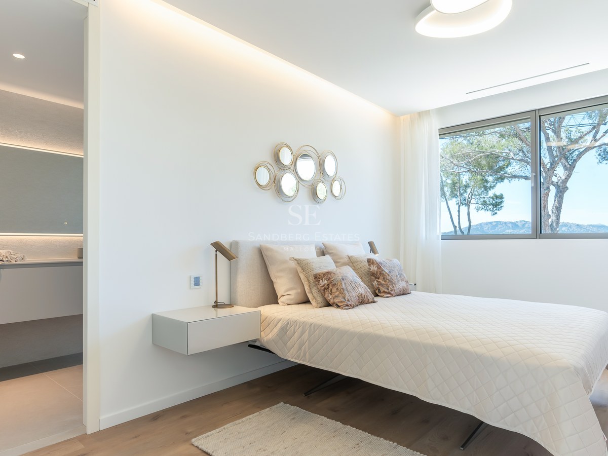 Bright bedroom featuring a queen bed, wooden floors, large windows with mountain views, and an ensuite bathroom.