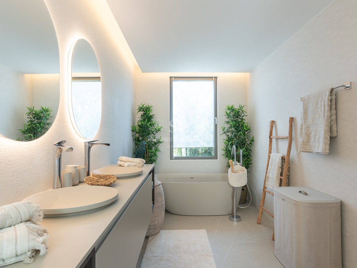 Contemporary master bathroom featuring backlit circular mirrors, dual sinks, a freestanding bathtub, and neutral decor.