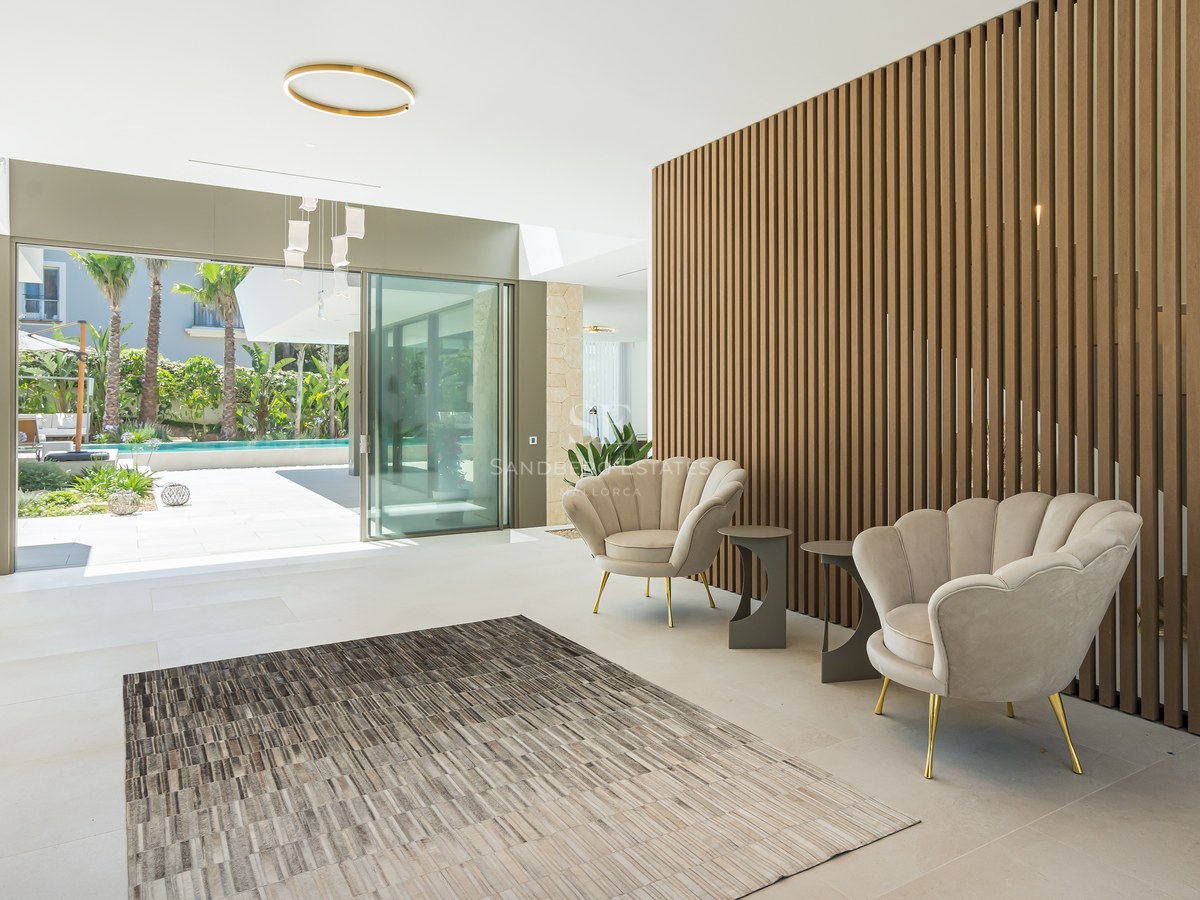 Modern lobby with wood slat wall, shell armchairs, and sliding glass doors opening to a pool and tropical garden.