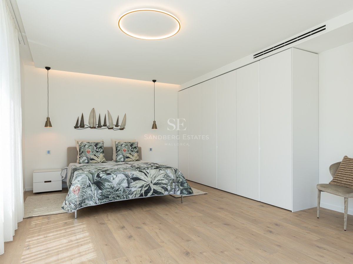 Bright contemporary bedroom featuring light wood floors, a large white wardrobe wall, and minimalist circular lighting.