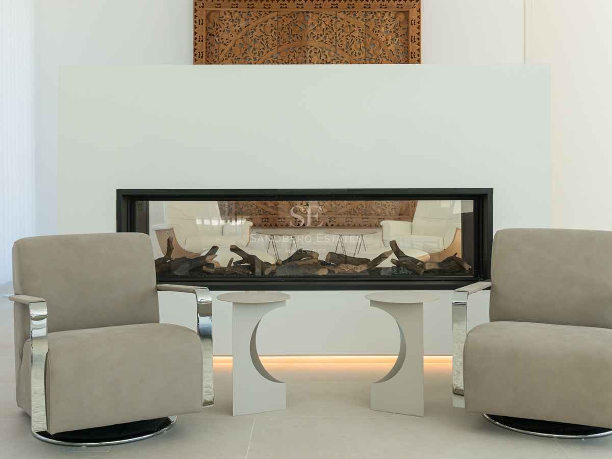Two modern taupe armchairs facing a built-in linear fireplace with a hand-carved decorative wood panel above.