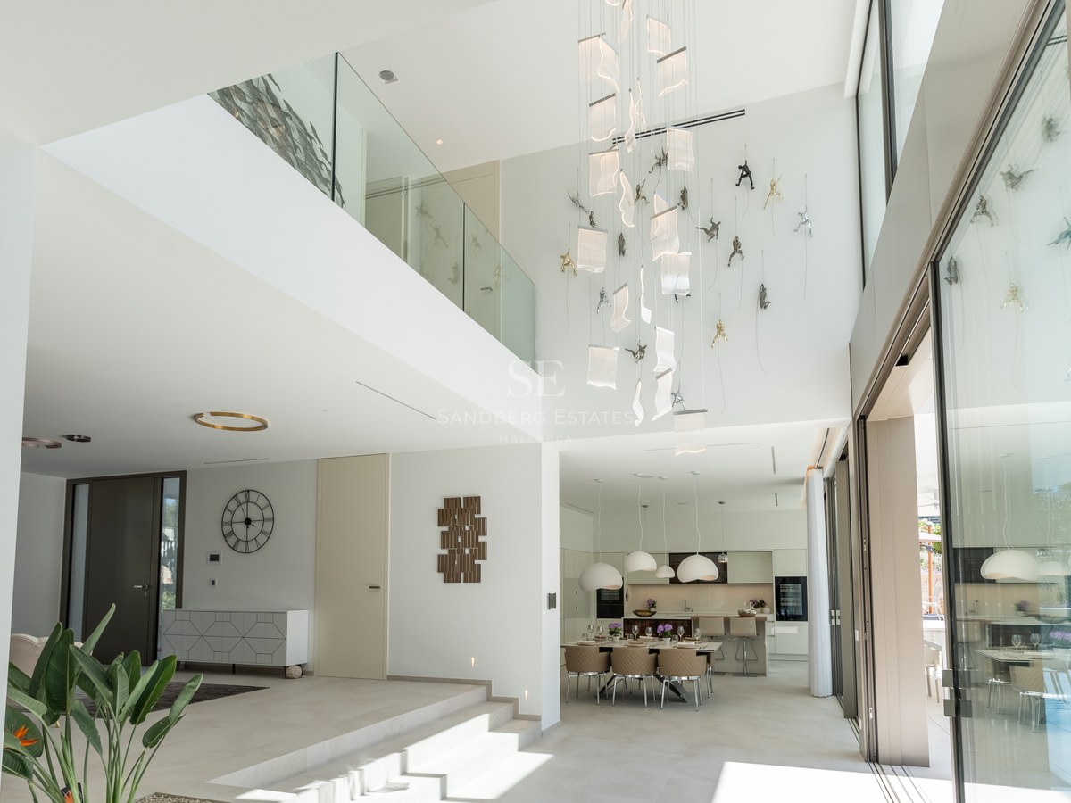 Bright double-height living space with glass balustrades, designer pendant lighting, and floor-to-ceiling windows.