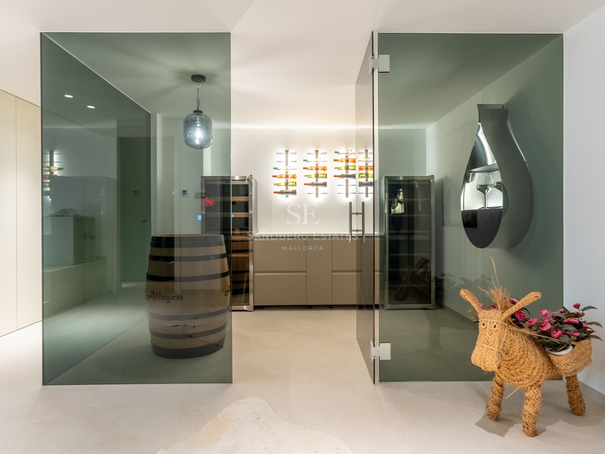 Contemporary wine cellar with glass doors, backlit bottle racks, climate cabinets, and a decorative wooden barrel.