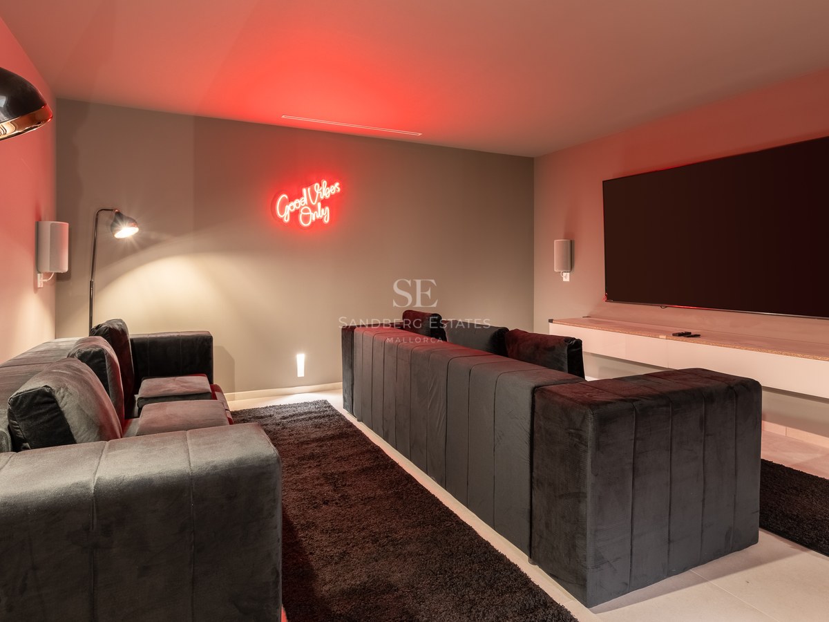 Home cinema room featuring deep charcoal velvet sofas, a large wall-mounted screen, and red neon wall art.