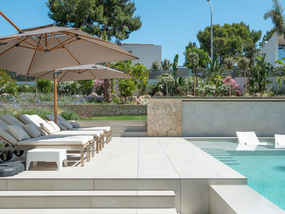 Modern swimming pool with in-water loungers and sun deck with parasols, surrounded by lush gardens.