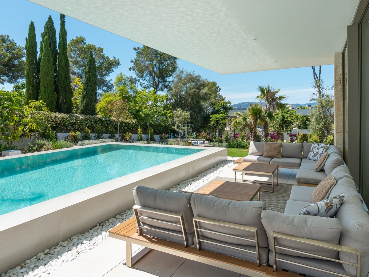 Raised infinity pool and gray lounge seating on a shaded terrace surrounded by lush Mediterranean greenery and mountain views.