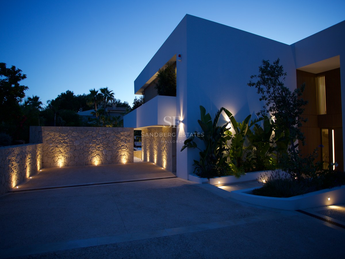 Modern white villa exterior featuring natural stone walls and integrated uplighting at dusk.