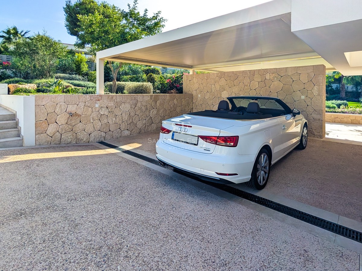 White convertible parked in a modern carport featuring natural stone walls and aggregate driveway beside stone stairs.