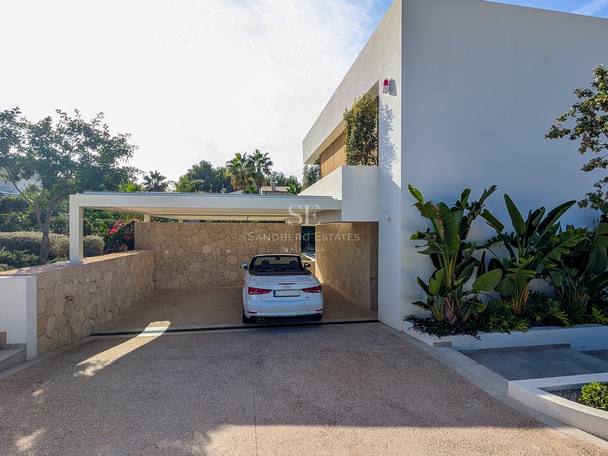 White convertible parked in a modern covered carport featuring natural stone walls and tropical landscaping.