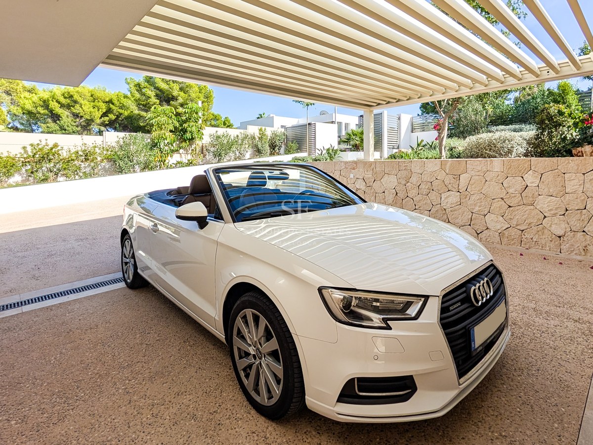 A white convertible car parked in a modern carport with a slatted roof and natural stone feature walls.