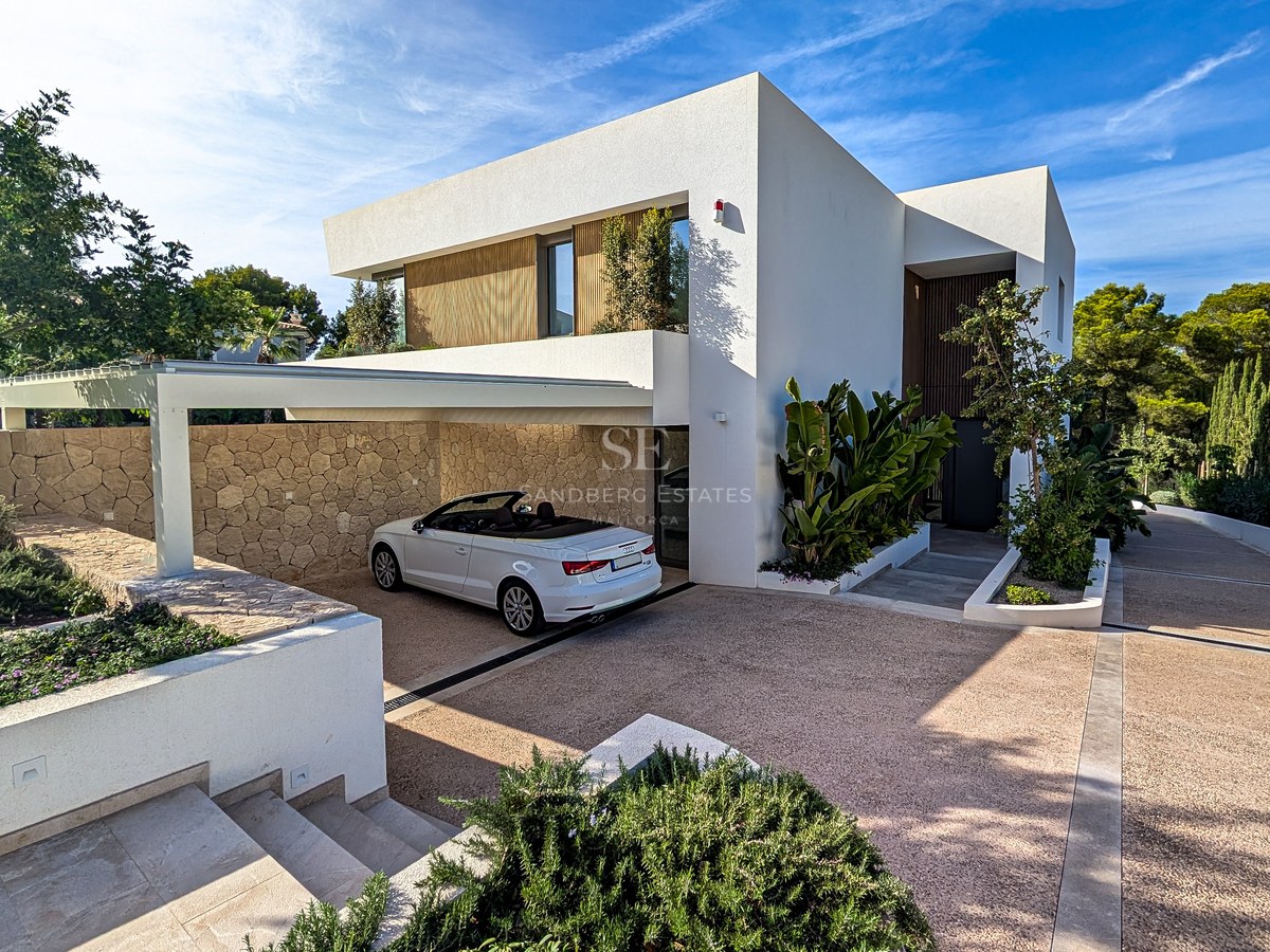 Modern white villa with a white convertible parked in a natural stone-walled carport under a clear blue sky.