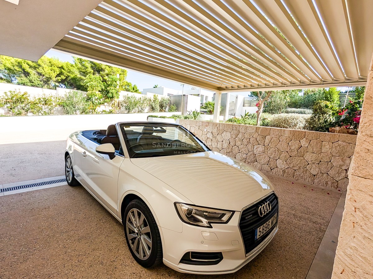 White convertible car parked under a modern slatted pergola next to a natural stone wall and garden greenery.