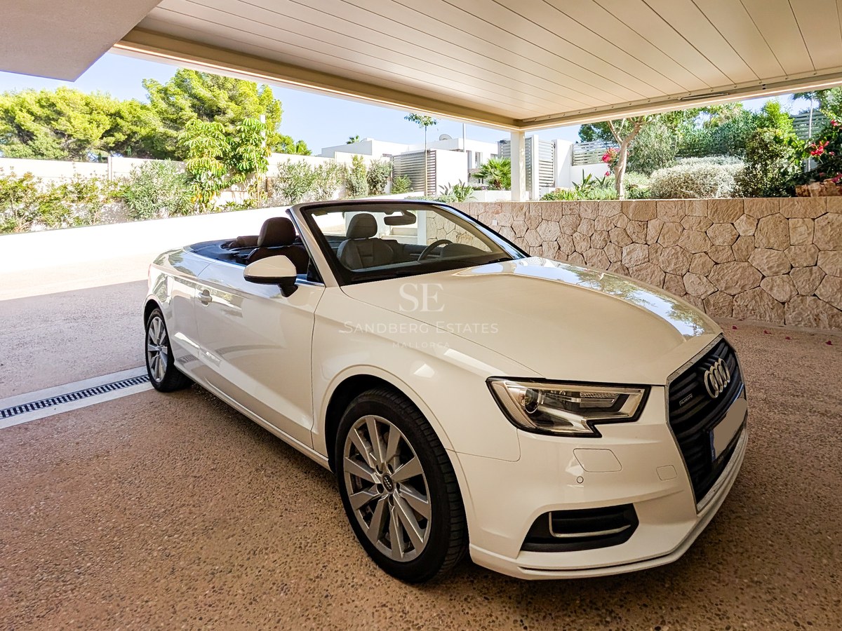 White convertible parked in a modern covered carport with natural stone walls and lush Mediterranean landscaping.