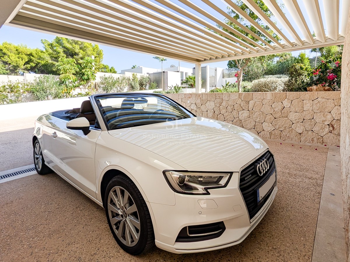 White convertible car parked under a modern slatted pergola next to a natural stone wall and lush garden.