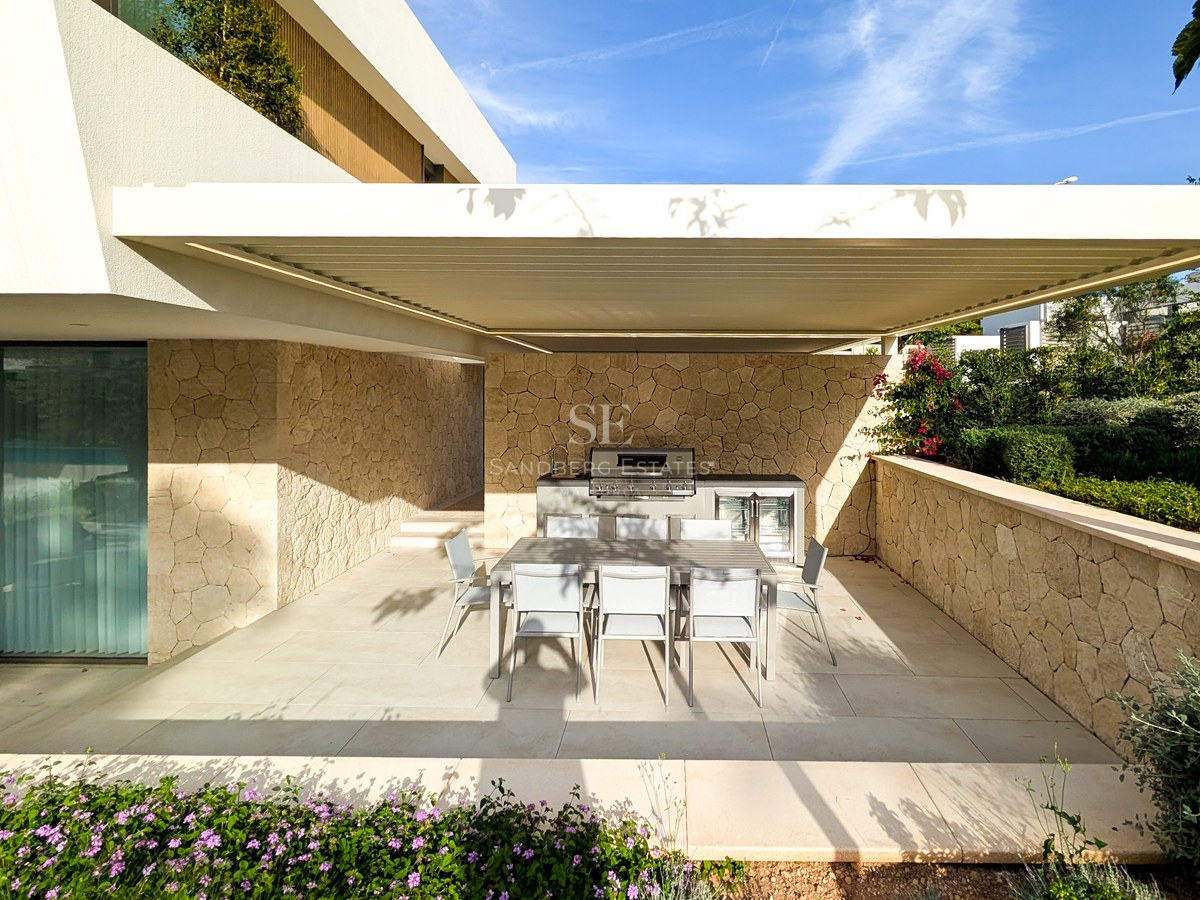Covered outdoor kitchen with stainless steel grill and dining table for eight against natural stone walls.