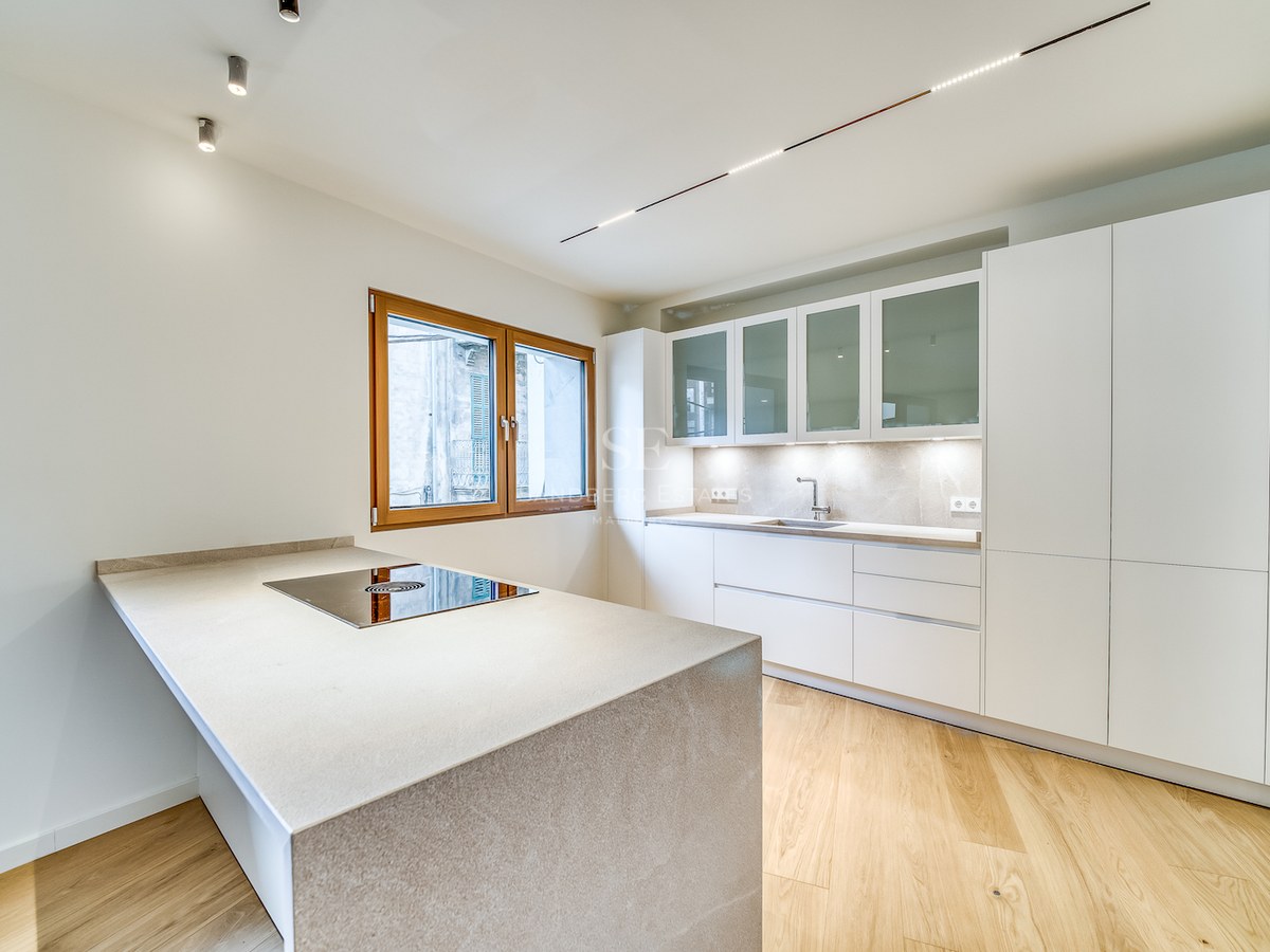 Cuisine moderne lumineuse avec îlot en pierre, plaque intégrée, armoires blanches et parquet en chêne.