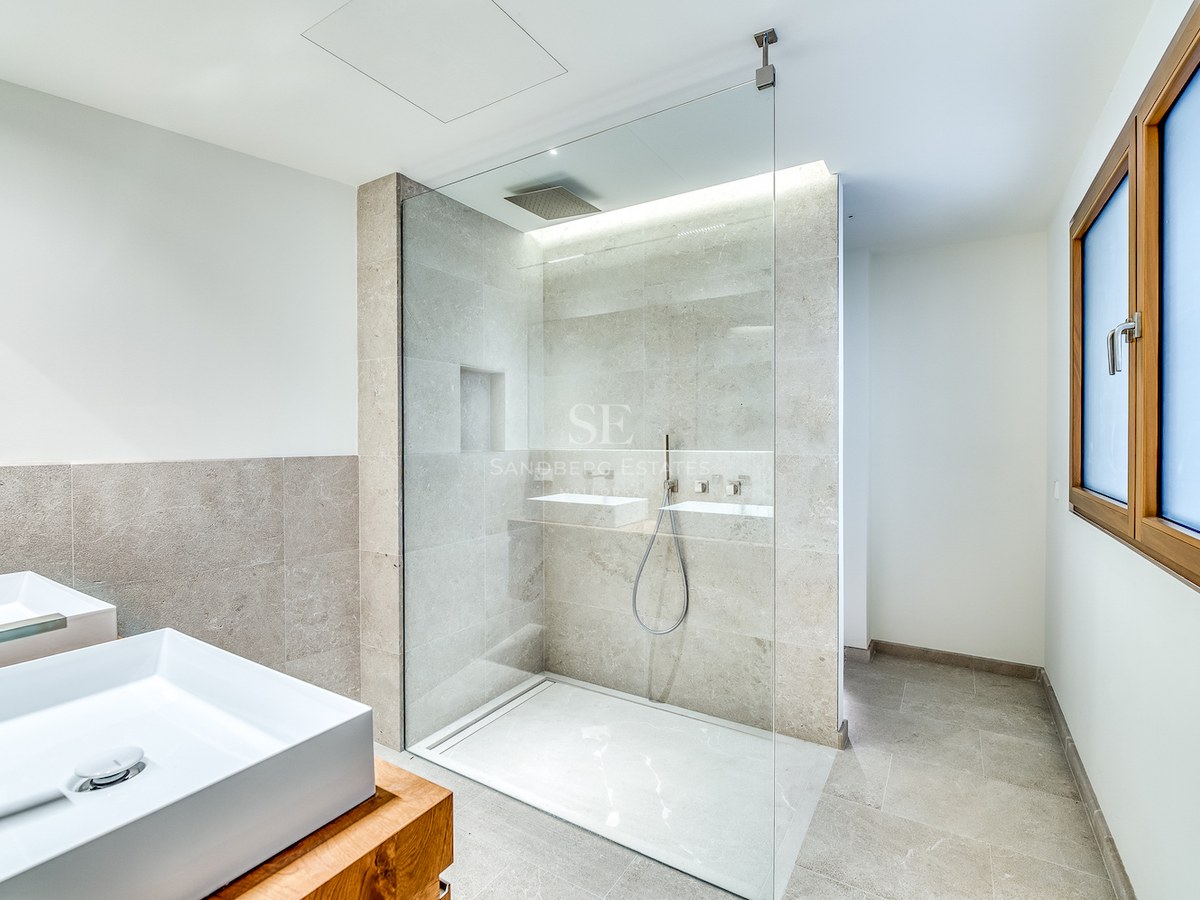 Salle de bain moderne avec douche vitrée, carrelage en pierre naturelle, double vasque et finitions en bois.