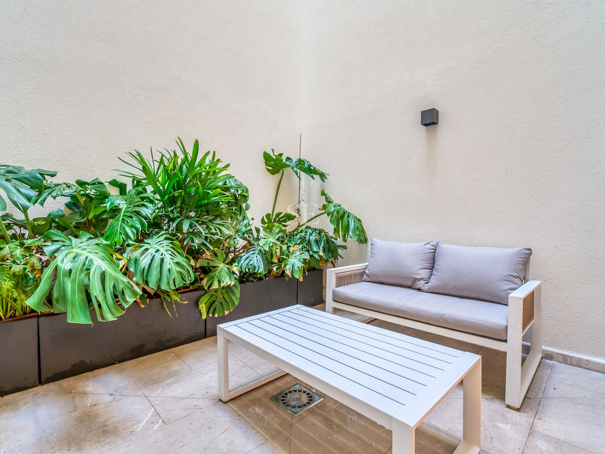Canapé et table basse blancs sur patio en pierre avec Monstera et murs crème.