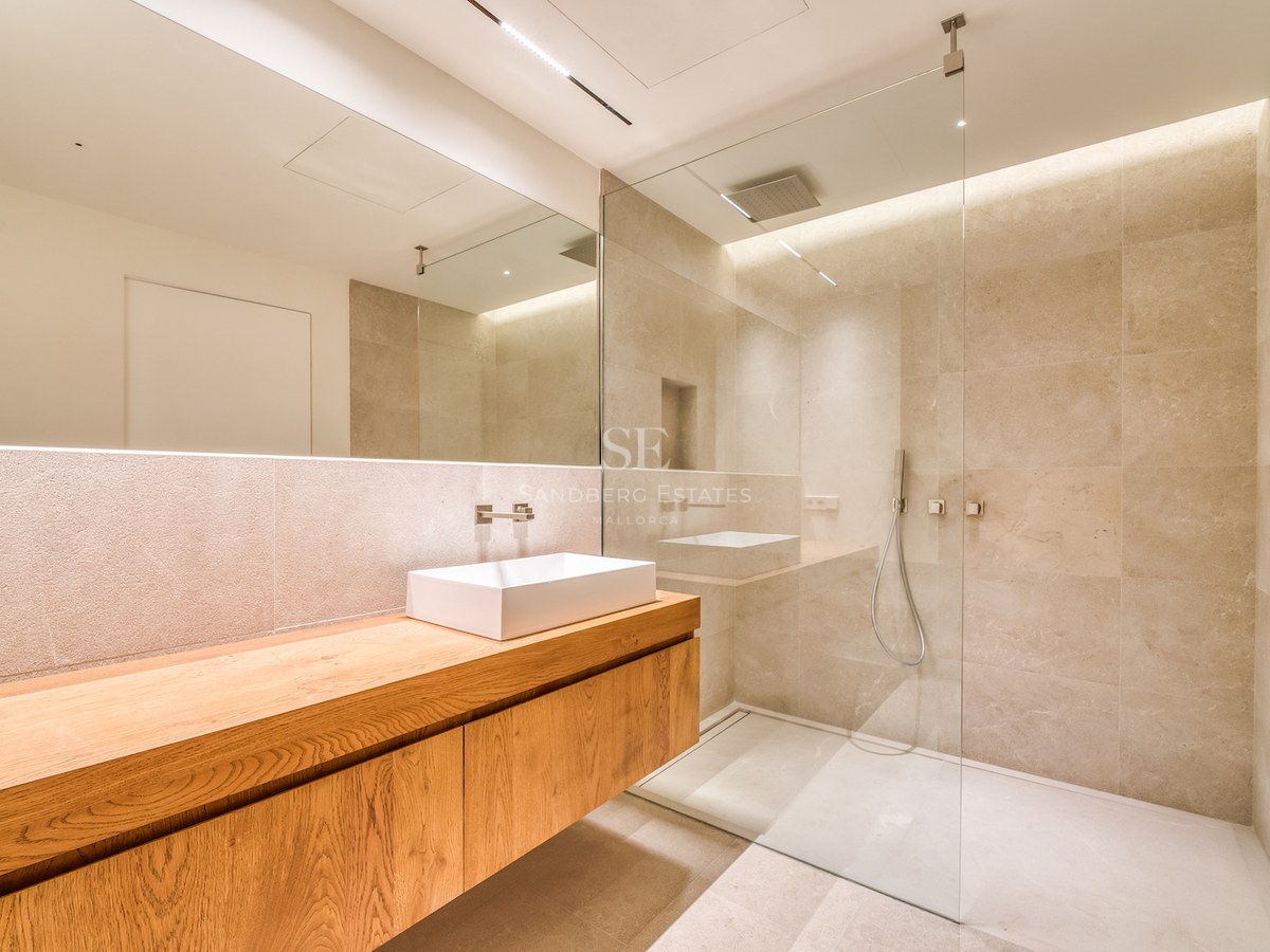 Salle de bain moderne avec meuble en chêne suspendu, vasque blanche, grand miroir et douche à l'italienne vitrée.