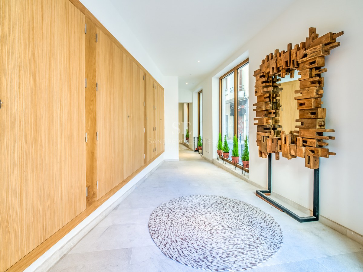 Couloir lumineux avec placards en chêne du sol au plafond, un miroir sculptural en bois et sol en pierre claire.