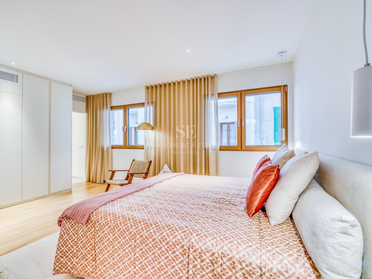 Chambre lumineuse avec grand lit, parquet en bois, placards intégrés blancs et menuiseries en bois.