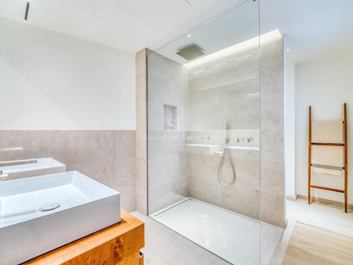 Salle de bains lumineuse avec deux vasques sur meuble en bois et une grande douche vitrée avec carrelage en pierre.