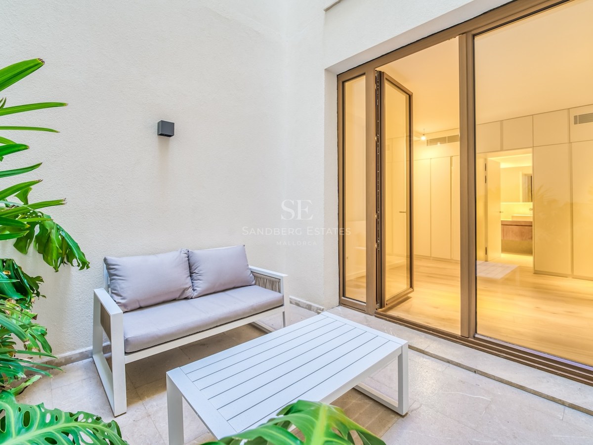 Petite terrasse privée avec mobilier moderne et baies vitrées menant à une chambre de maître contemporaine.
