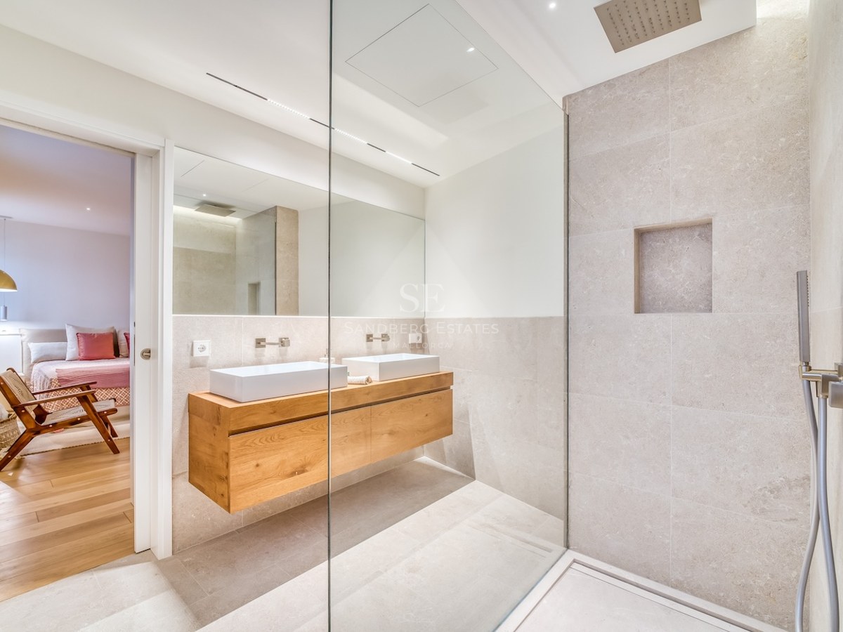 Salle de bains moderne avec douche à l'italienne, double vasque sur meuble en bois et carrelage en pierre beige.