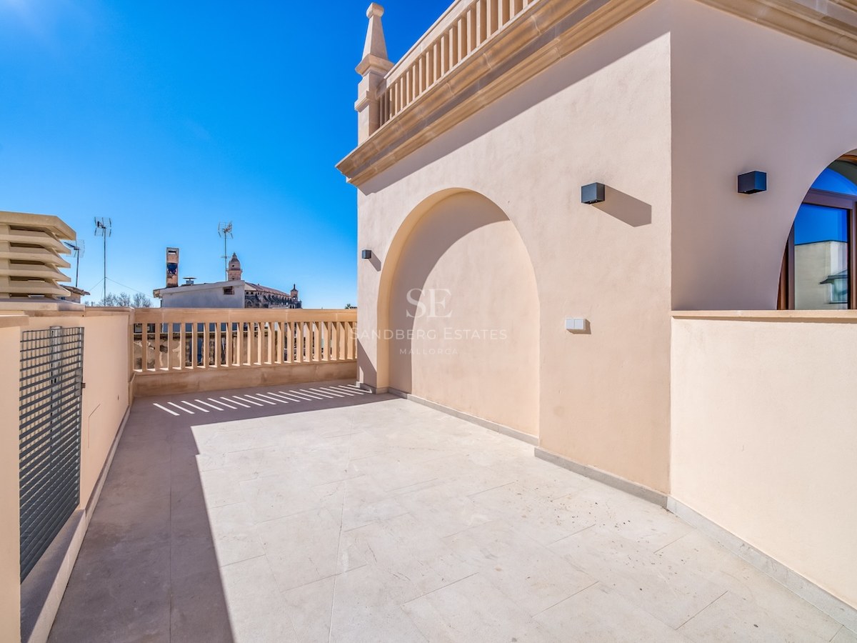 Grande terrasse de toit en pierre naturelle avec alcôve en arche et balustrade classique sous un ciel bleu dégagé.