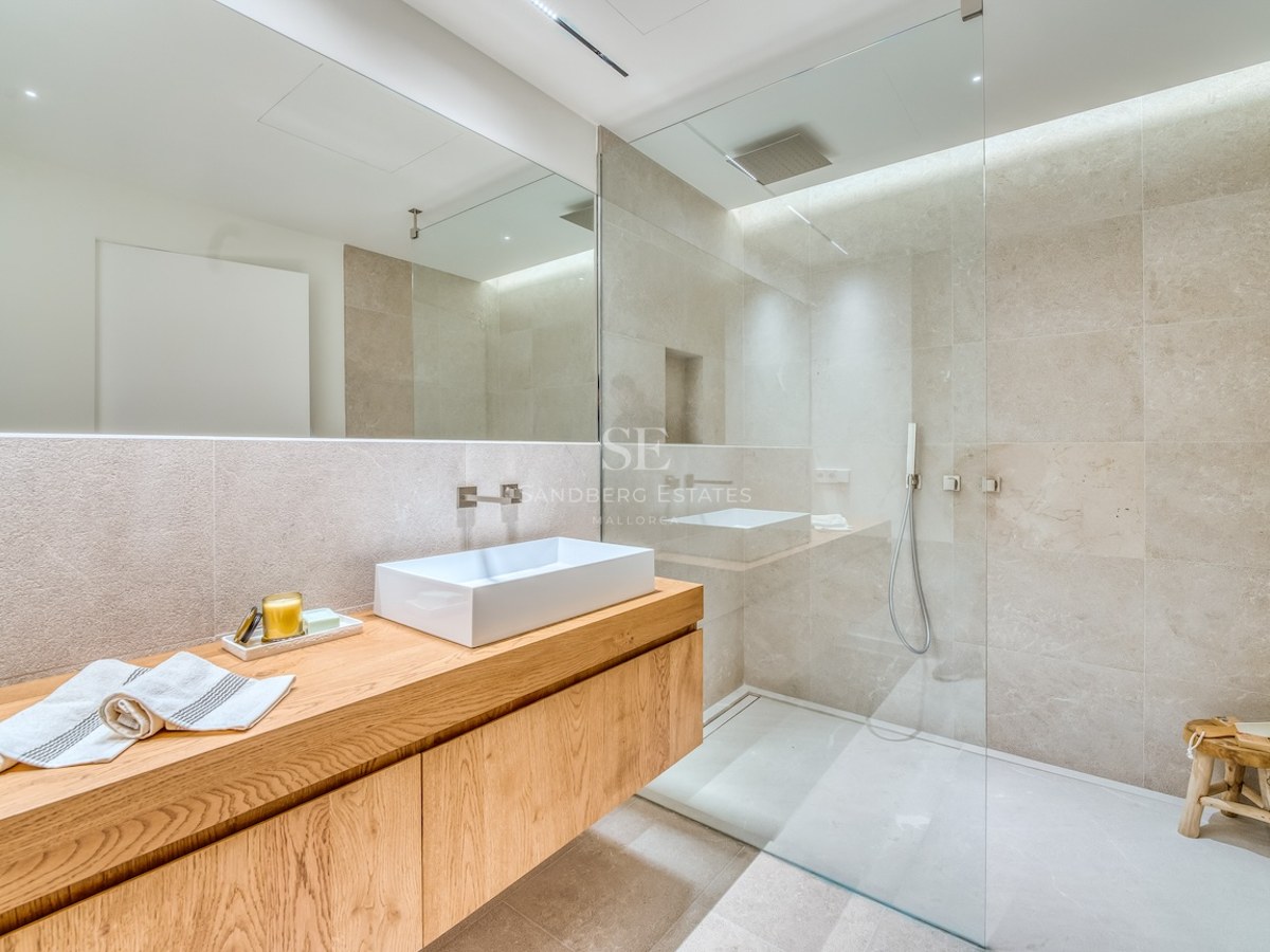 Salle de bain moderne avec meuble en chêne, vasque blanche et douche vitrée aux murs en pierre.