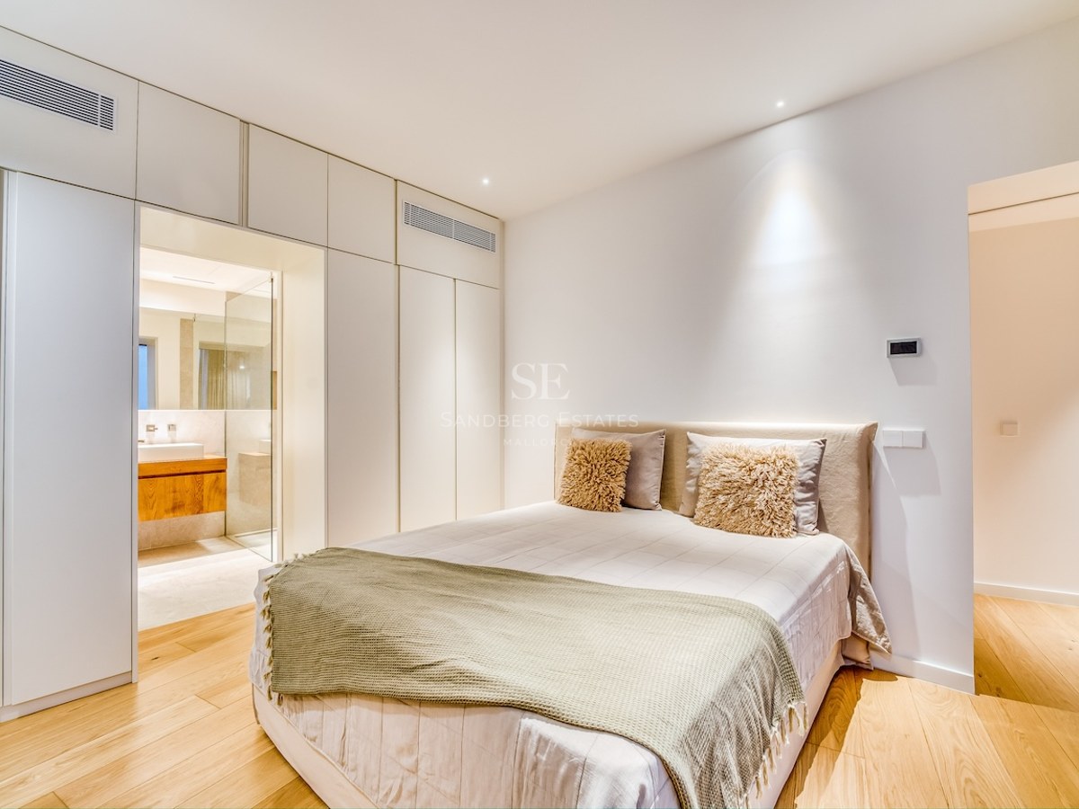 Chambre moderne avec lit double, placards intégrés blancs, parquet en chêne et vue sur la salle de bain en suite.