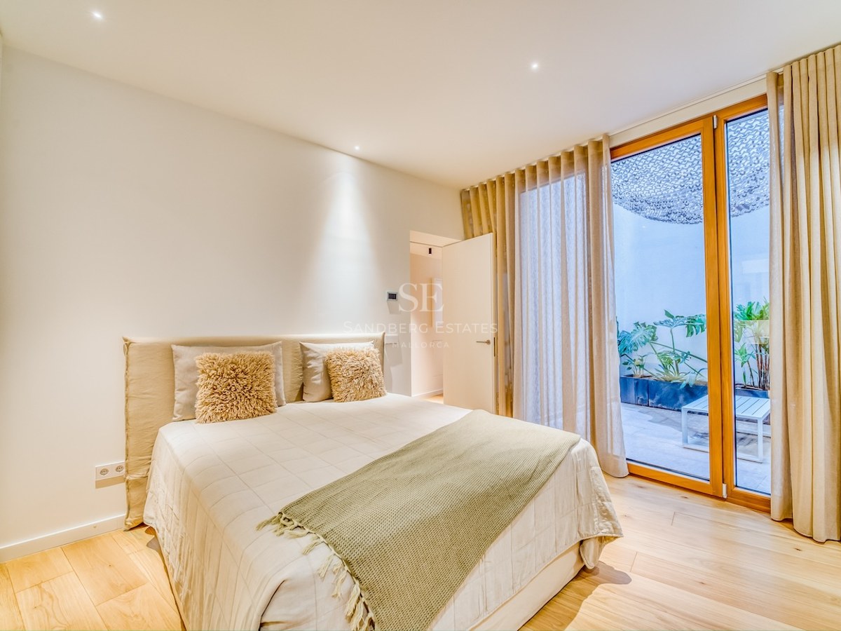 Chambre lumineuse avec parquet, literie neutre et baies vitrées ouvrant sur un patio arboré.