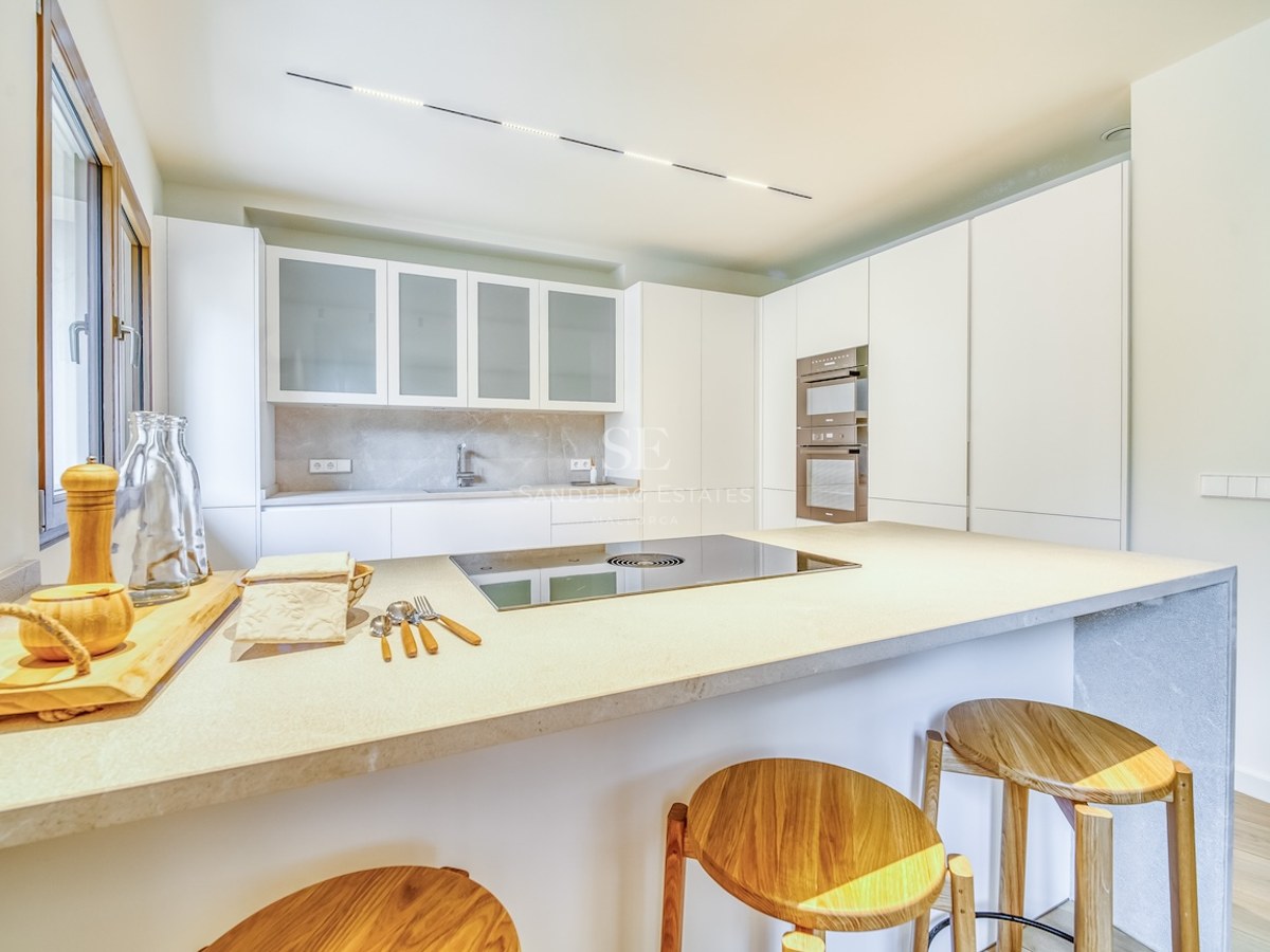 Cuisine minimaliste lumineuse avec placards blancs, îlot en pierre avec tabourets en bois et appareils intégrés.