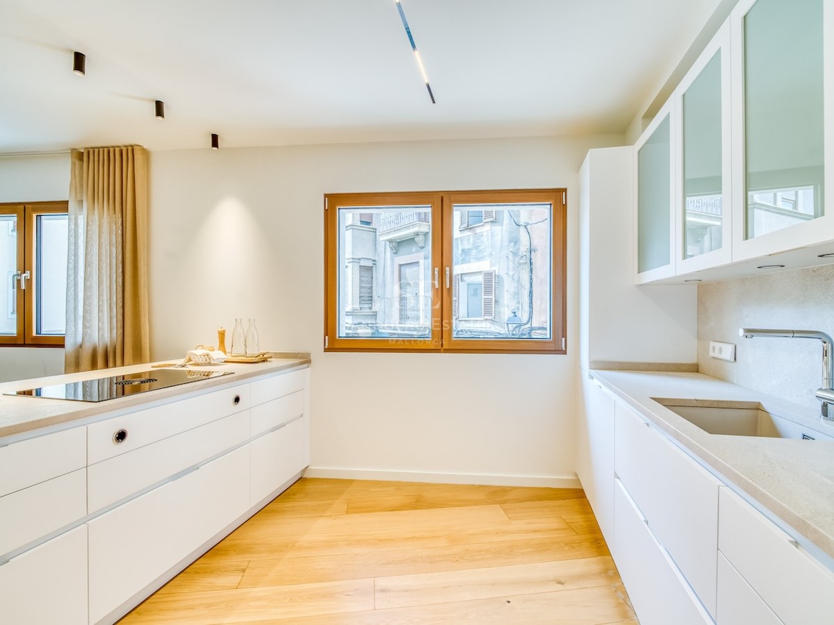 Cuisine blanche moderne avec parquet en chêne, plans de travail en quartz et fenêtres en bois.