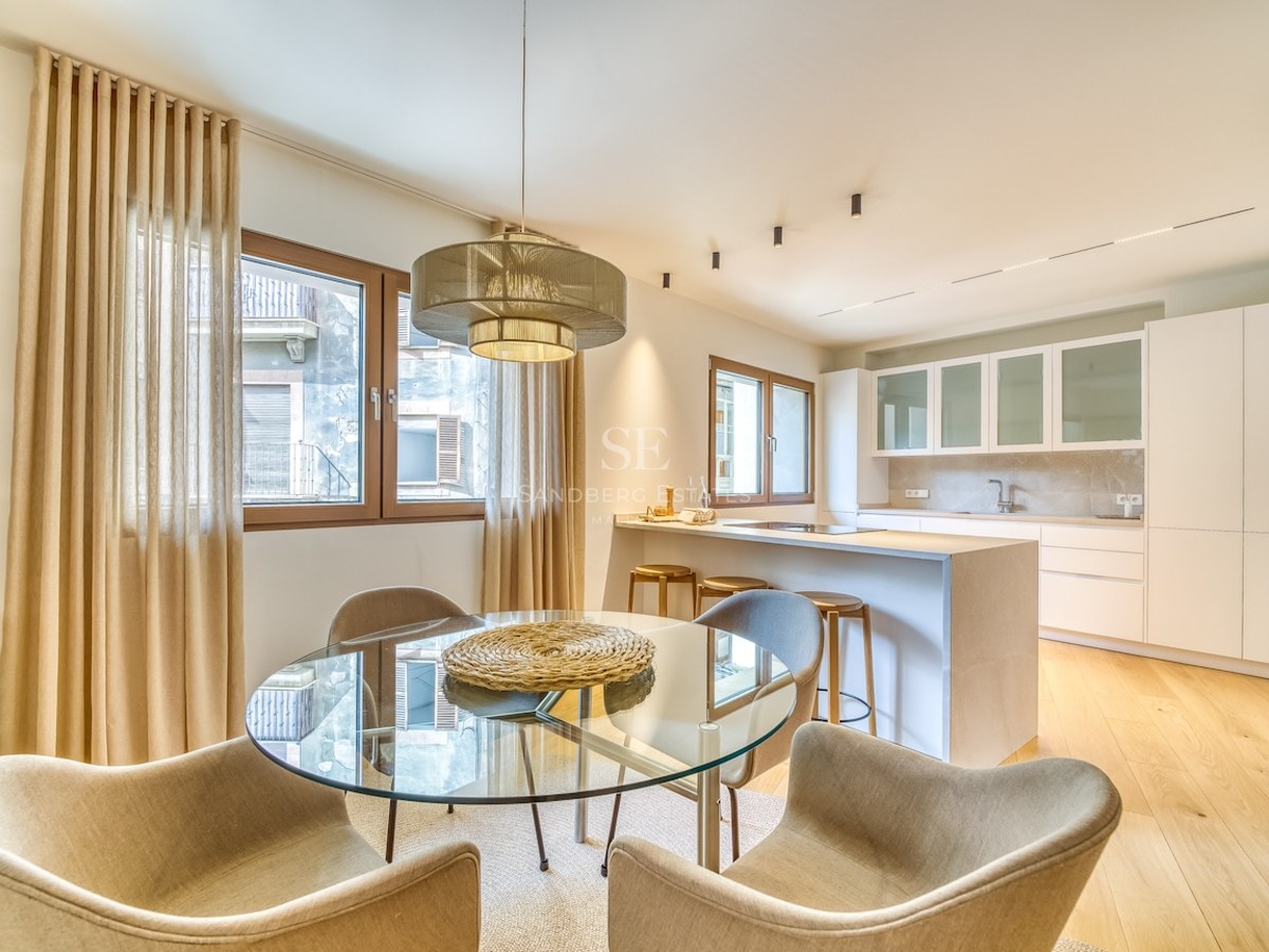Cuisine moderne ouverte avec placards blancs, îlot en bois avec tabourets et table à manger ronde en verre.
