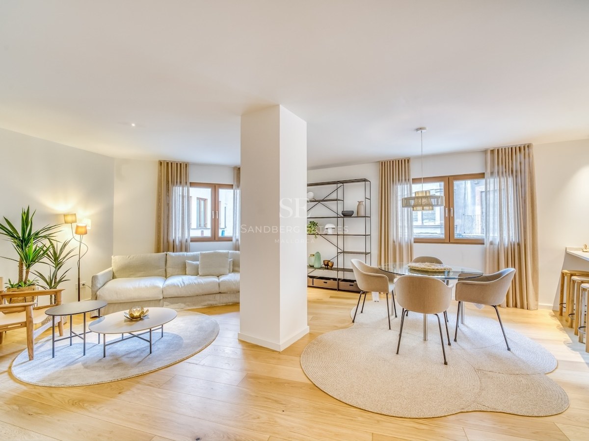 Salon spacieux à aire ouverte avec parquet en chêne clair, mobilier neutre et coin repas intégré.