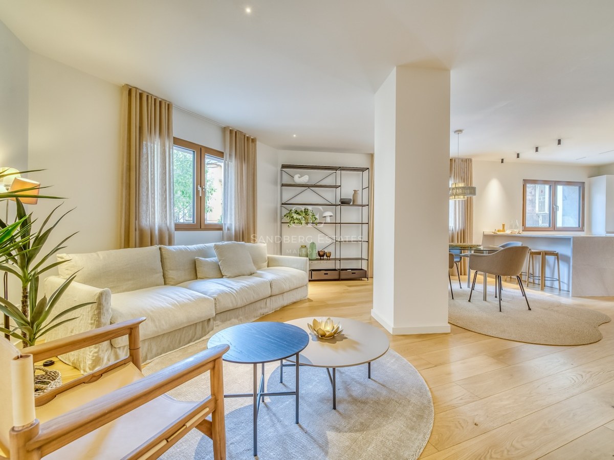 Salon lumineux à aire ouverte avec parquet en chêne clair, canapé crème et espaces cuisine et salle à manger intégrés.