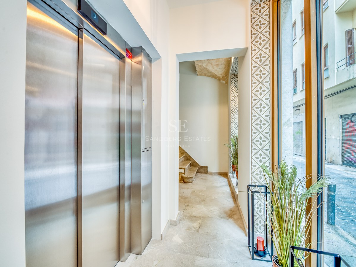 Entrée moderne avec ascenseur en acier inoxydable, sol en pierre naturelle et grande baie vitrée donnant sur la rue.