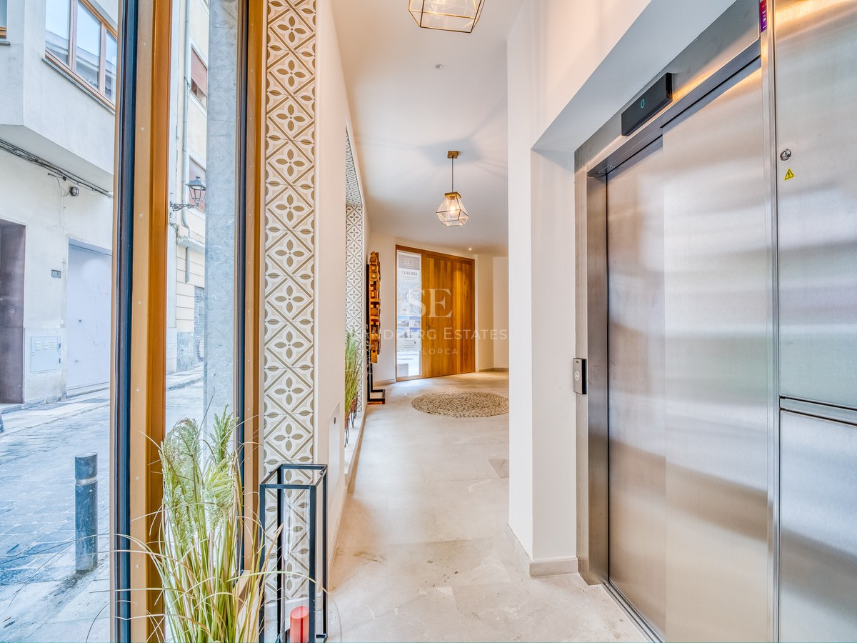 Hall d'entrée lumineux avec ascenseur en acier inoxydable, sol en pierre naturelle et carreaux décoratifs.