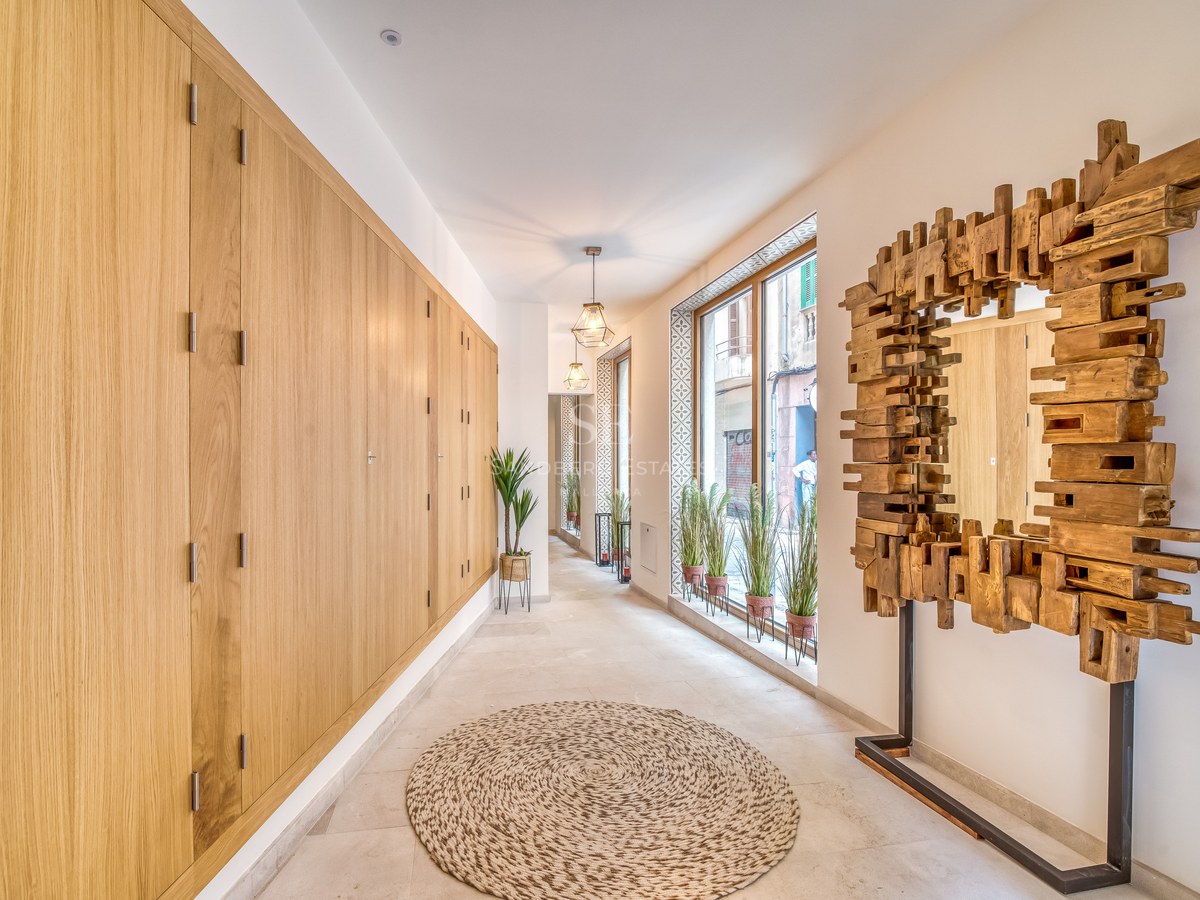 Couloir lumineux avec rangements en chêne du sol au plafond, miroir sculptural en bois et grandes fenêtres.