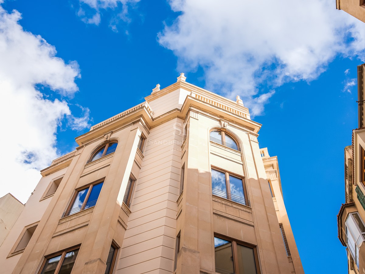 Vue en contre-plongée d'une façade en pierre beige avec fenêtres cintrées en bois sous un ciel bleu vif.
