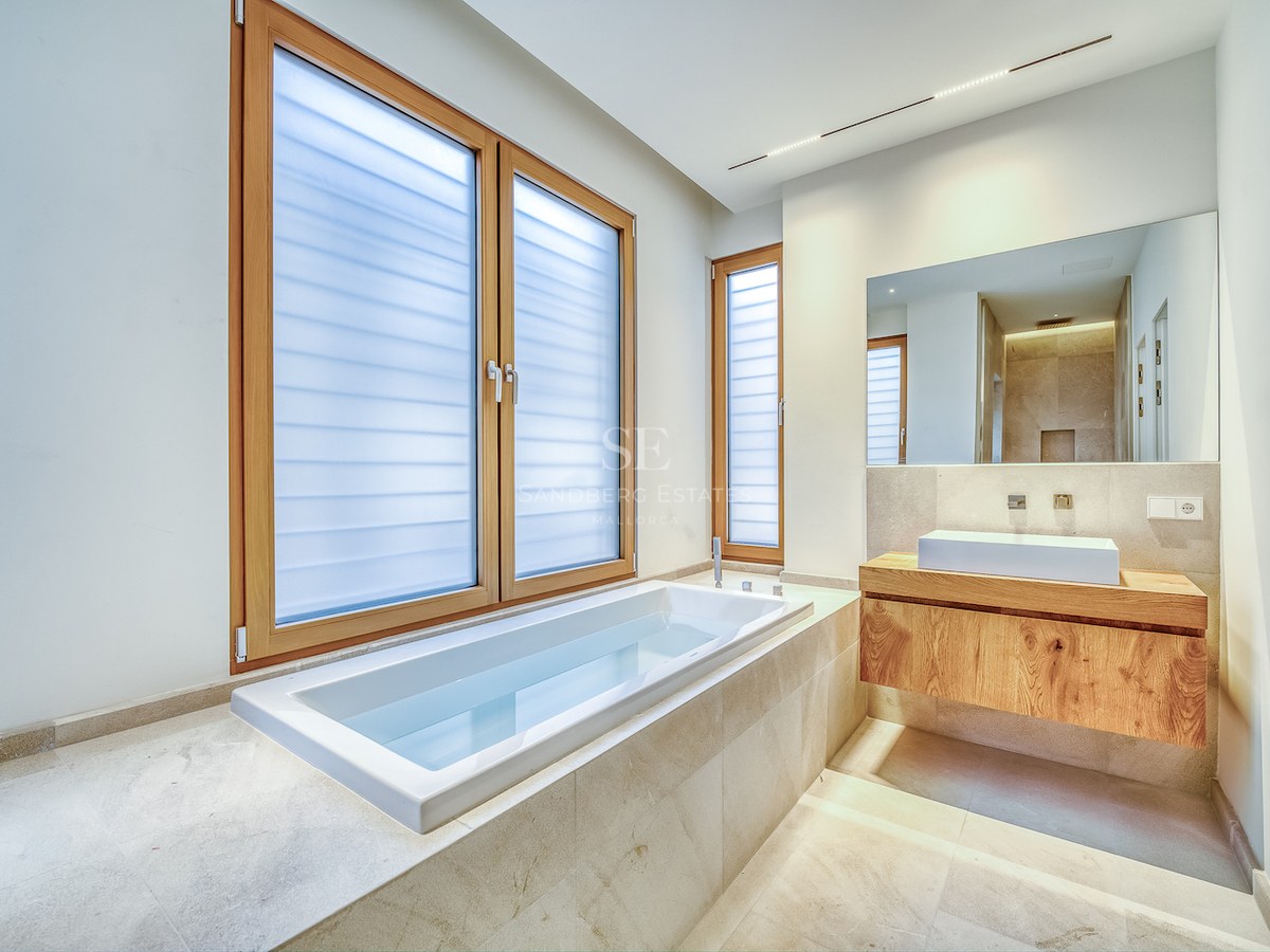 Salle de bains moderne avec baignoire encastrée, meuble vasque en chêne et grandes fenêtres.