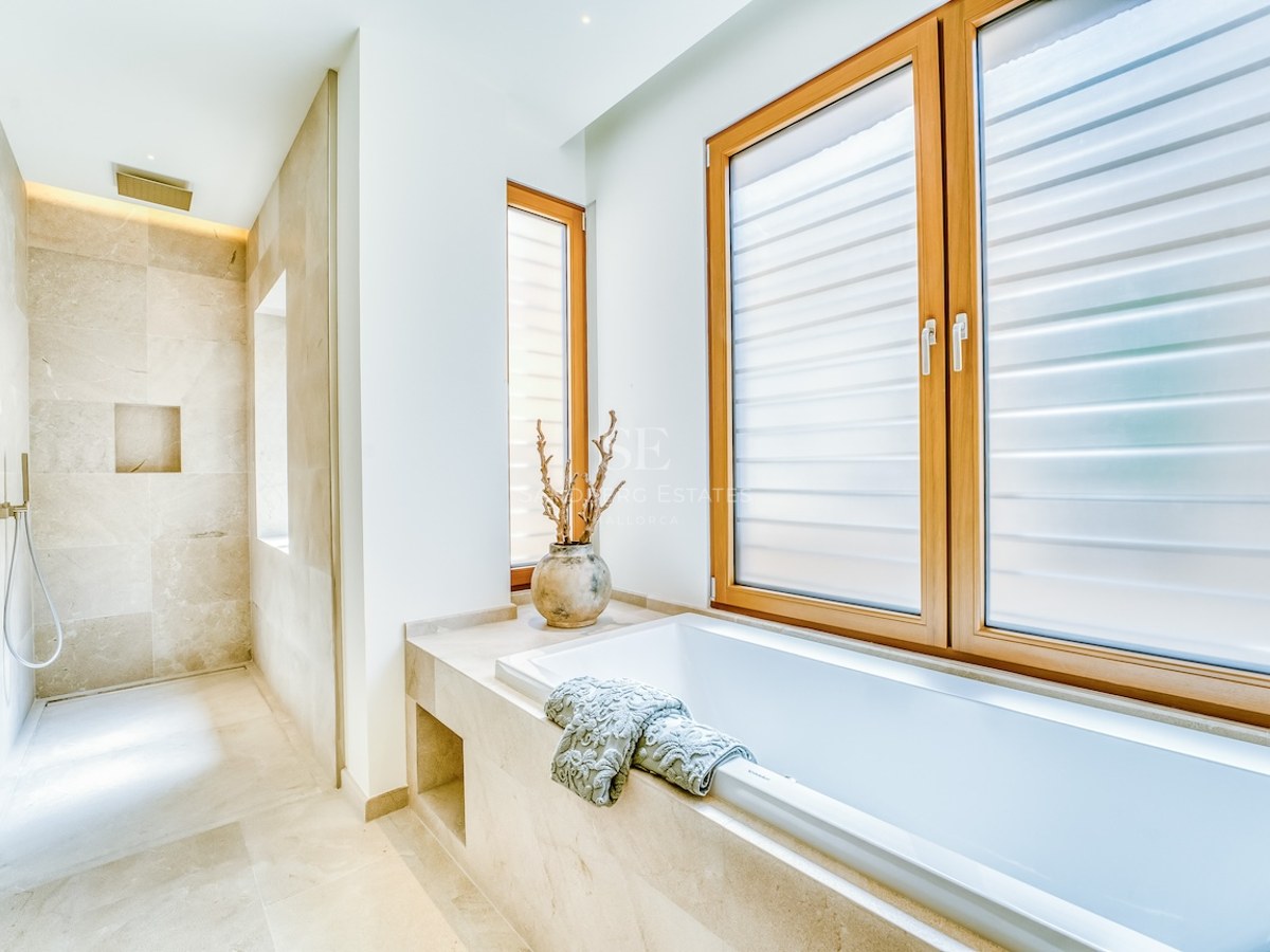Modern bathroom featuring a built-in bathtub, walk-in rain shower, and natural stone tiling with oak window frames.