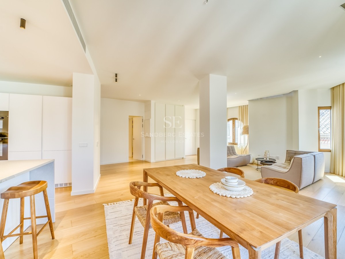 Bright open-plan living room featuring a light oak dining set, white minimalist kitchen, and floor-to-ceiling windows.