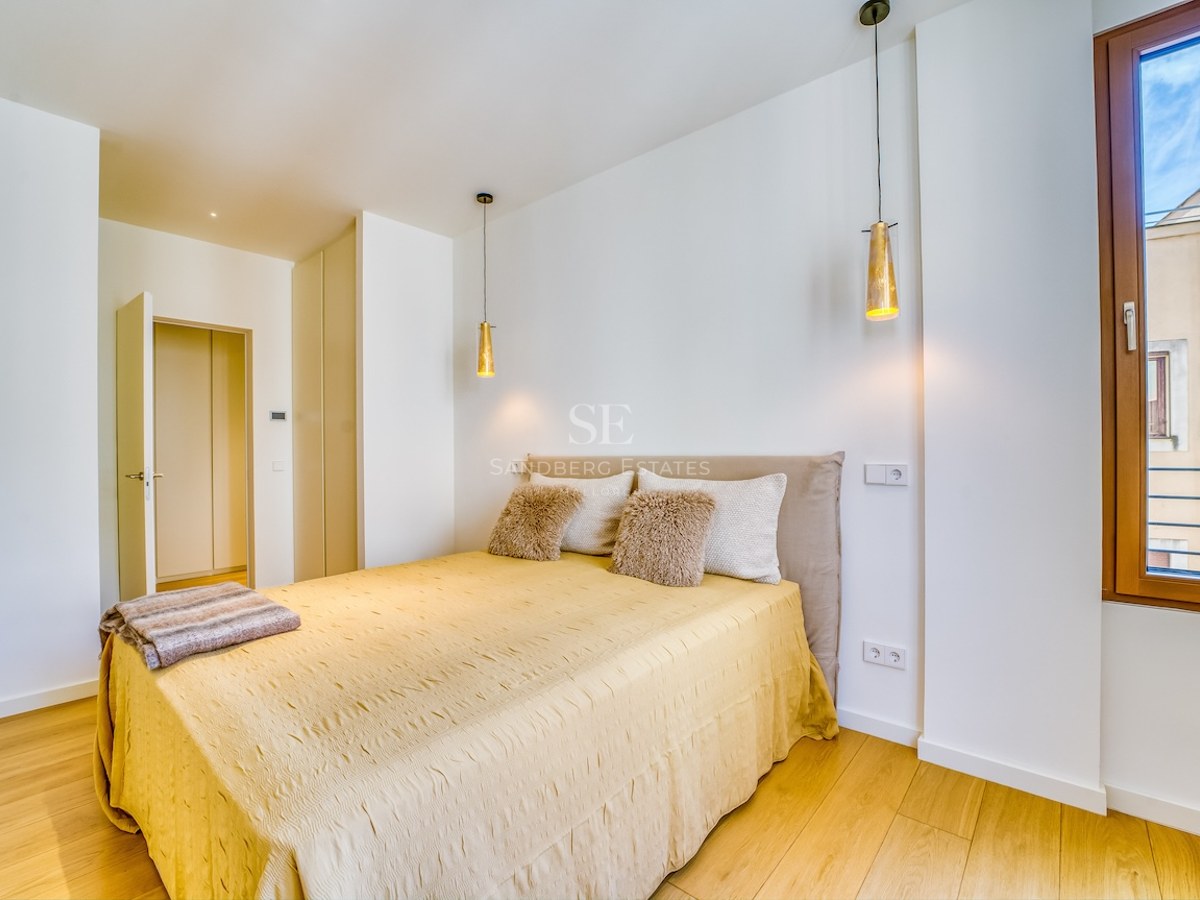 Bright bedroom featuring light wood floors, a bed with a yellow cover, and two gold pendant lamps by a window.