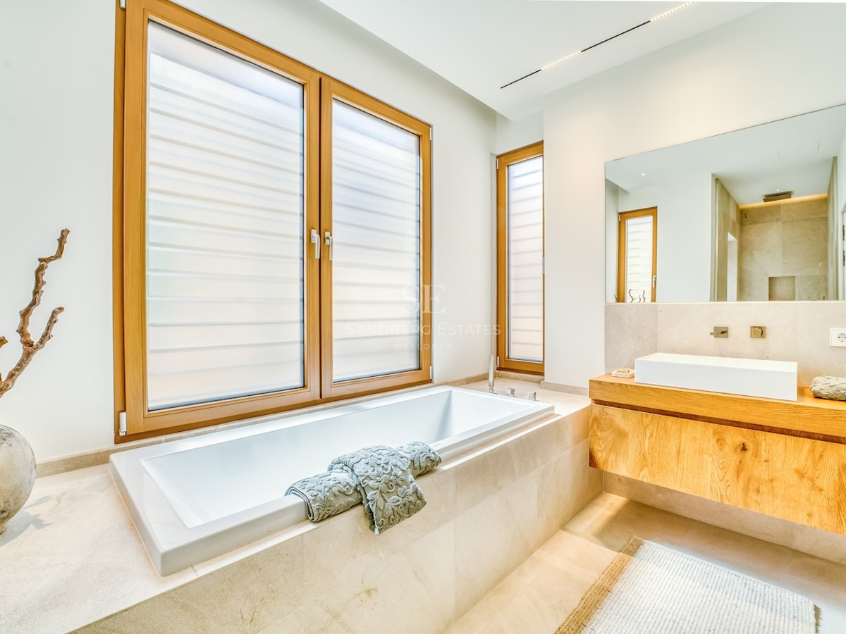 Minimalist bathroom featuring a built-in white bathtub, oak floating vanity, and natural stone tiling.