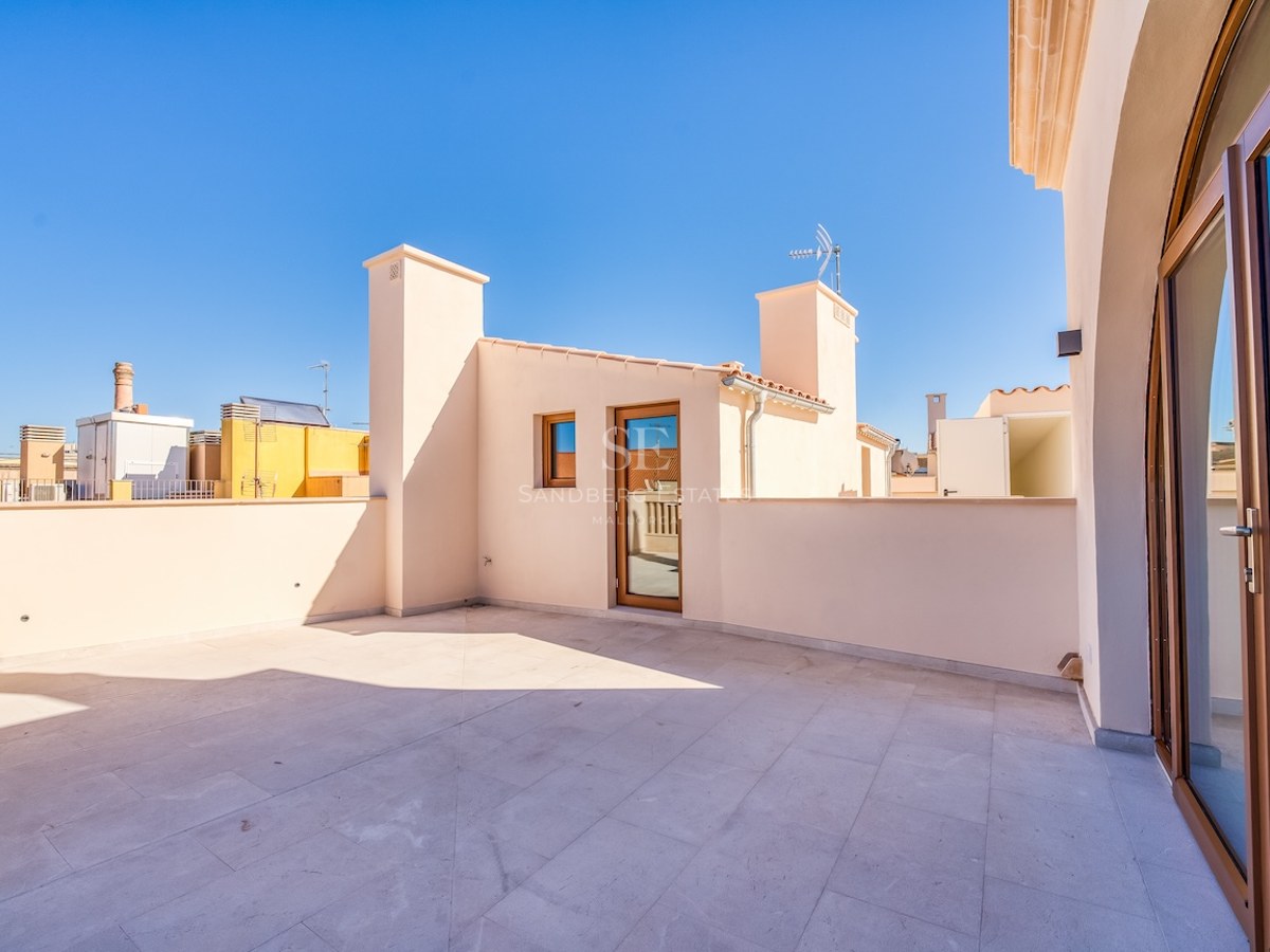 Large rooftop terrace with natural stone tiling and cream walls under a clear blue sky.